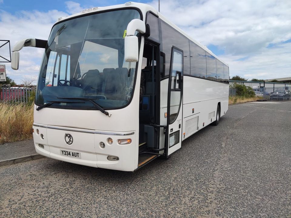 White coach seen from the front with its door open, parked on tarmac