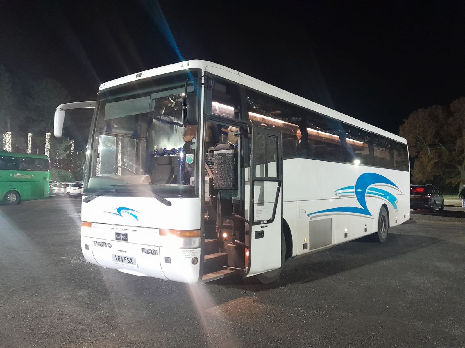White coach with a blue swoosh lit up at night with its door open on a car park